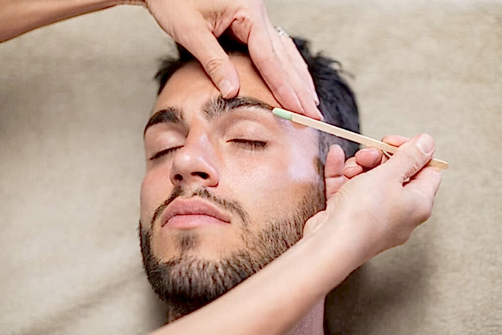 Hombre con esteticista depilando sus cejas con cera