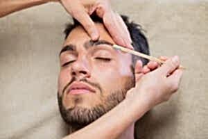 Hombre con esteticista depilando sus cejas con cera